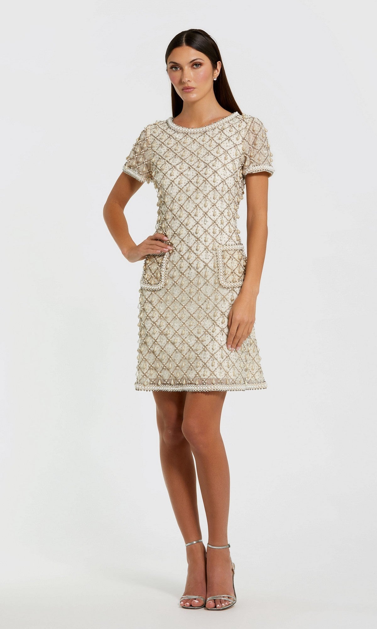 A woman poses against a plain background in the Mac Duggal 10097 short semi-formal dress in Oyster with short sleeves, knee-length textured fabric featuring a subtle diamond pattern, paired with metallic heels.